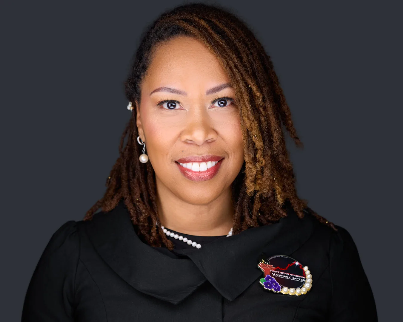 Professional headshot of a smiling Northern Virginia executive in a black jacket with a pearl necklace on a dark studio backdrop