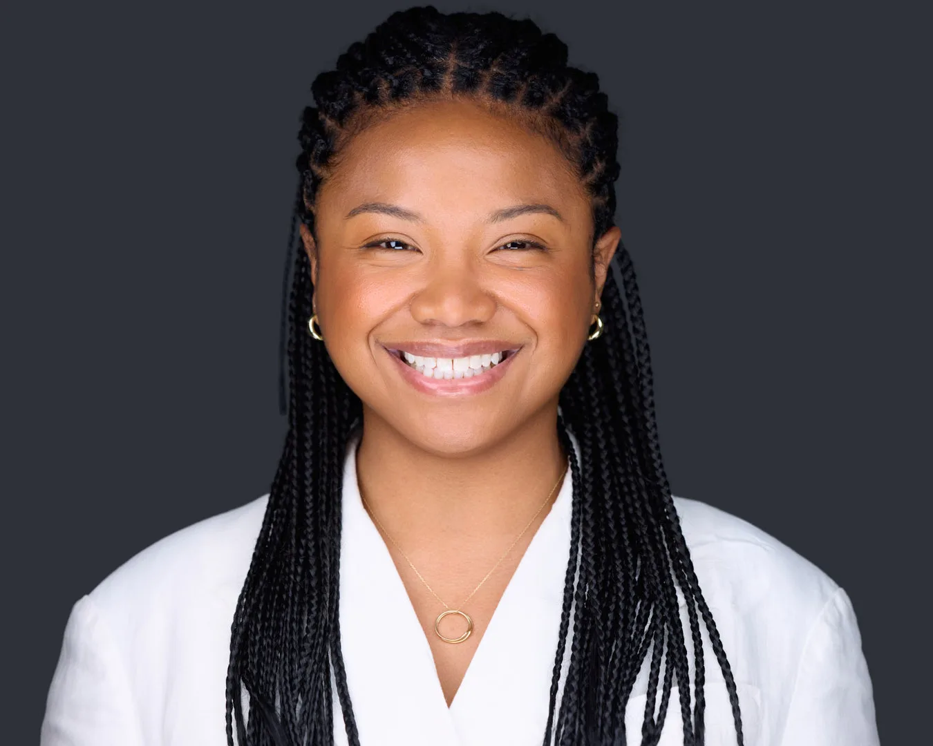 Professional headshot of a woman with braids smiling naturally in a white blazer