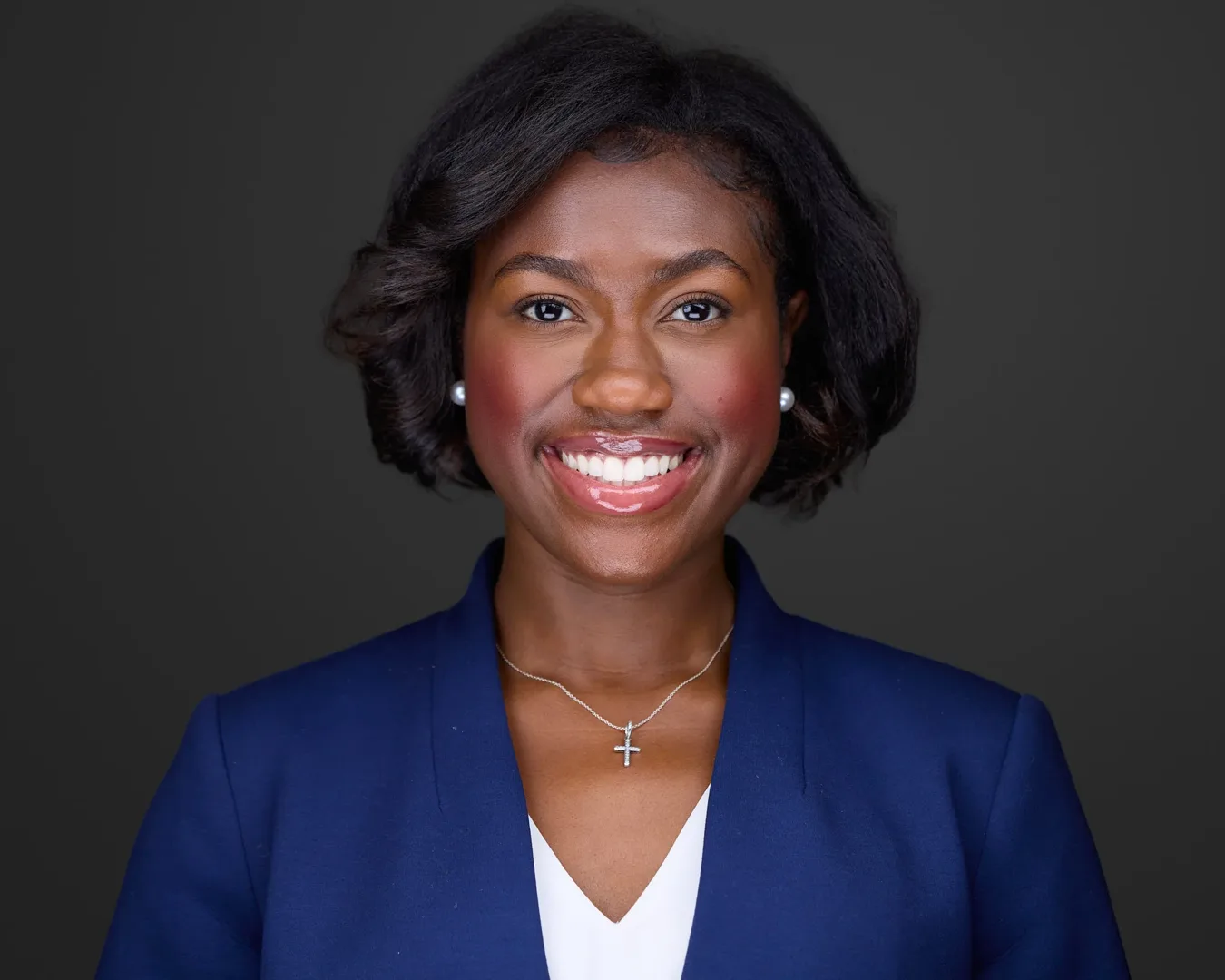 Professional headshot of a smiling woman in a navy blazer and pearl earrings