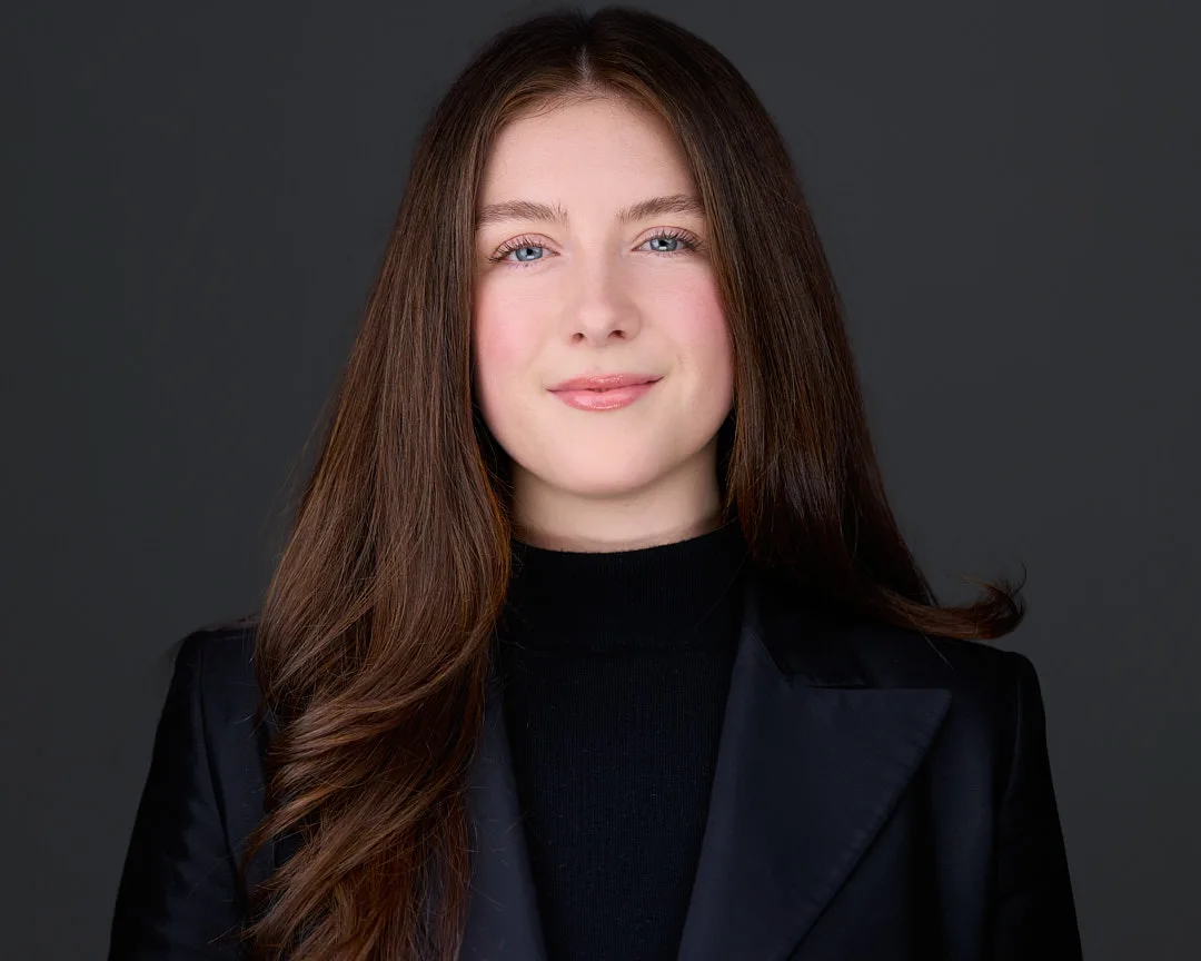 Professional headshot of a businesswoman in a black turtleneck and blazer on a dark studio backdrop