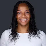 J. Miller professional headshot in white top with twist braids against dark studio backdrop