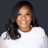 M. Miller professional headshot in white top with long dark waves against dark studio backdrop